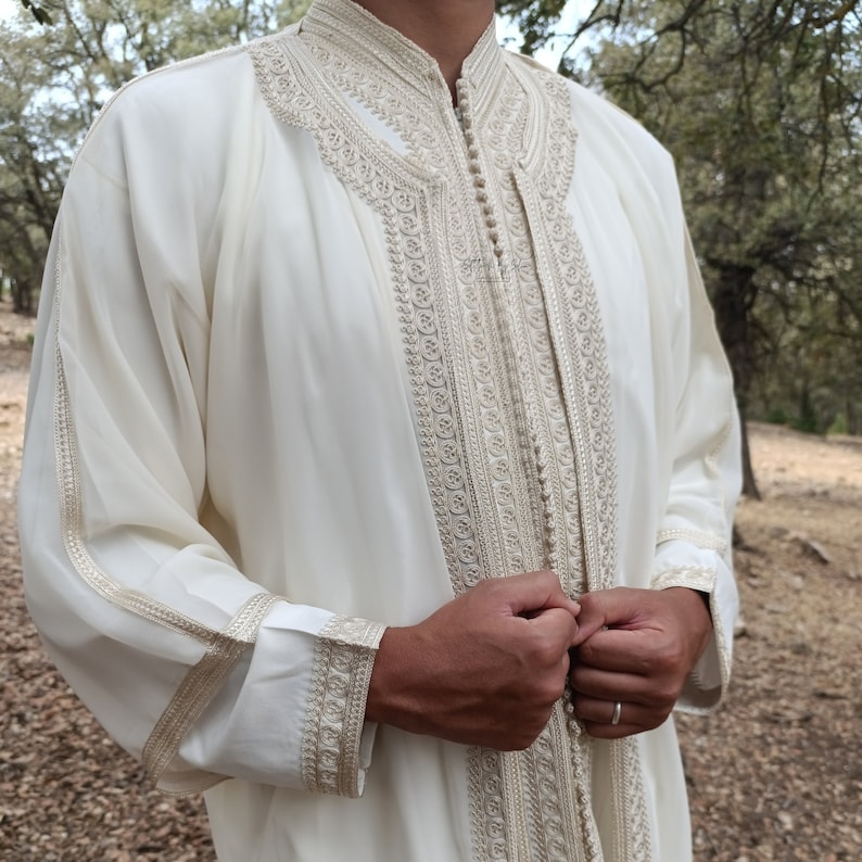 May include: A white long-sleeved robe with intricate gold embroidery around the collar, cuffs, and front closure. The robe is made of a lightweight fabric and has a relaxed fit.
