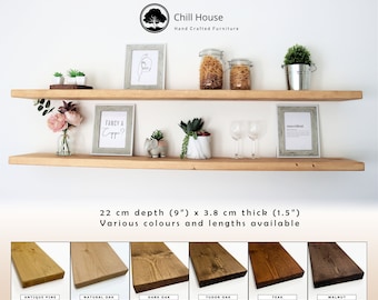 May include: Two wooden shelves, 9 inches deep and 1.5 inches thick, are mounted on a white wall. The shelves are made of reclaimed wood and have a natural finish. The shelves are decorated with various items, including plants, glasses, and framed artwork. The text "Fancy a Capp?" and "smarcident" are visible on the shelves. The image shows six different wood finishes for the shelves: Antique Pine, Natural Oak, Dark Oak, Tudor Oak, Teak, and Walnut.
