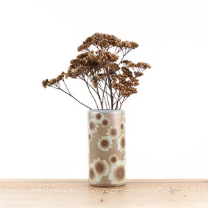 Può includere: Un vaso in ceramica marrone con un motivo floreale bianco e marrone, pieno di fiori secchi marroni.