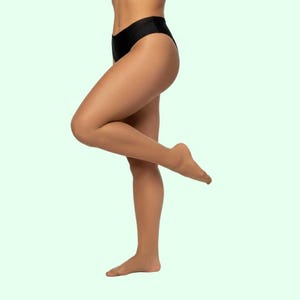 May include: Black underwear. A person is standing with one leg raised, showcasing the underwear. The background is a light green color. The underwear is high-waisted and appears to be made of a smooth fabric.