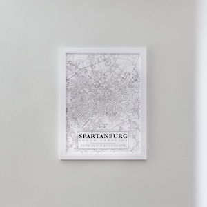 May include: A black and white line art map print of Spartanburg, South Carolina. The print is framed in a white frame and includes the city's name, state, and coordinates.