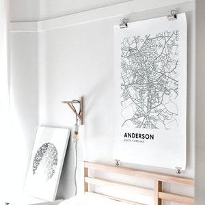 May include: A black and white map print of Anderson, South Carolina, hanging on a white wall above a wooden bed frame.