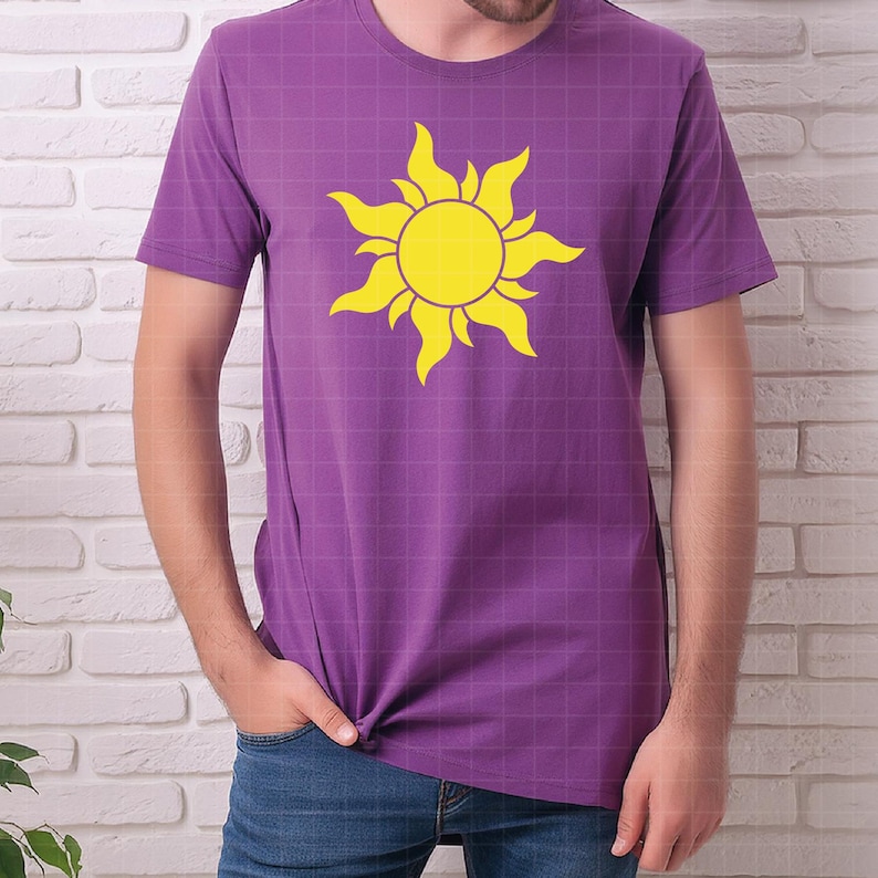 May include: A purple short-sleeved t-shirt featuring a large, bright yellow sun graphic centered on the chest. The sun design has a circular center with stylized, flame-like rays extending outward in a circular pattern across the front of the shirt.