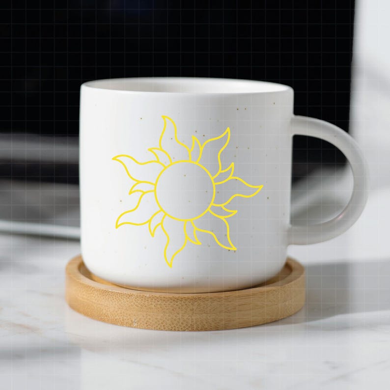 May include: A white ceramic mug featuring a yellow sun graphic with stylized flame-like rays. The mug has a smooth finish and a curved handle, resting on a circular light brown wooden coaster that matches the diameter of the mug base.