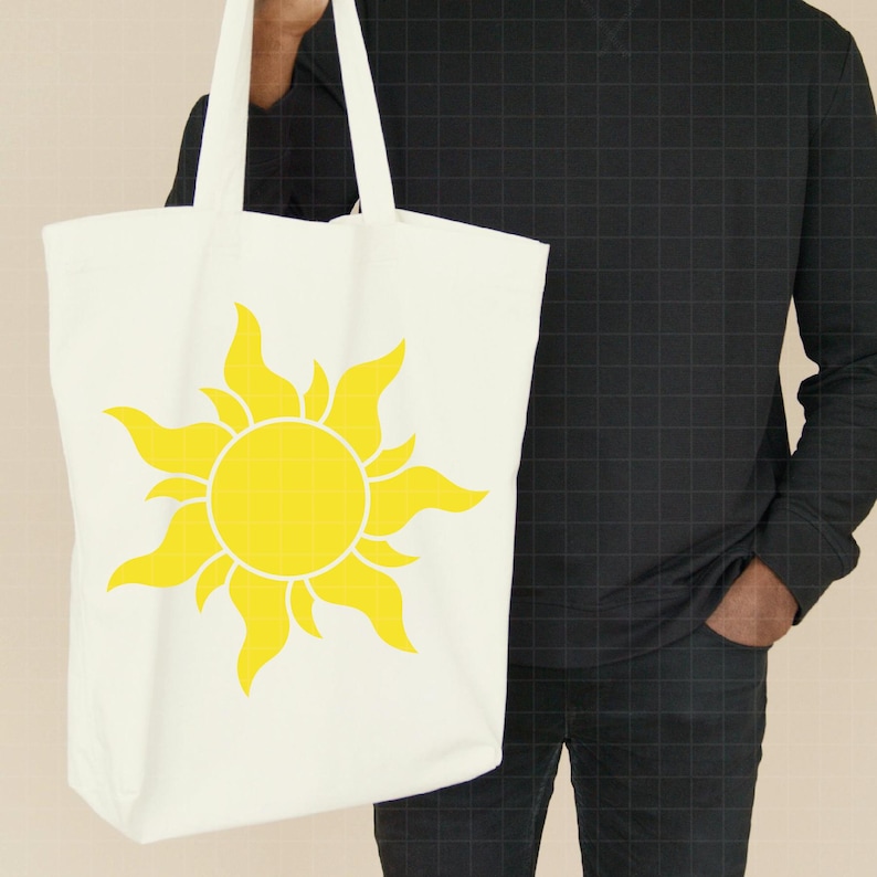 May include: A white canvas tote bag featuring a large, bright yellow sun graphic printed on the front. The sun design has a central circular core surrounded by stylized, flame-like rays extending outward in a symmetrical pattern across the bag.