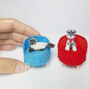 May include: Two miniature crocheted chairs, one blue with a white cat sitting on it and one red with a gray dog sitting on it.