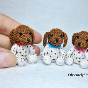 May include: Three small crocheted brown and white spotted dog figurines wearing different colored collars. The dogs are sitting on a white surface.