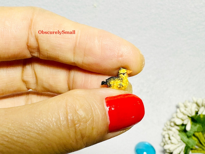 Op de afbeelding: Een klein, gehaakt geel eendje met zwarte ogen en een zwarte snavel. Het eendje zit op een vinger.