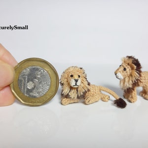 Pu&ograve; includere: Due miniature di leoni in crochet, una marrone e una beige, con volti bianchi e occhi neri. I leoni sono seduti accanto a una moneta canadese da un dollaro per la scala.