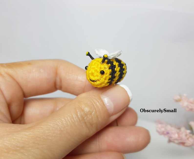 Op de afbeelding: Een kleine gehaakte bij met zwarte en gele strepen, witte vleugels en zwarte kraaloogjes. De bij wordt in de hand van een persoon gehouden.