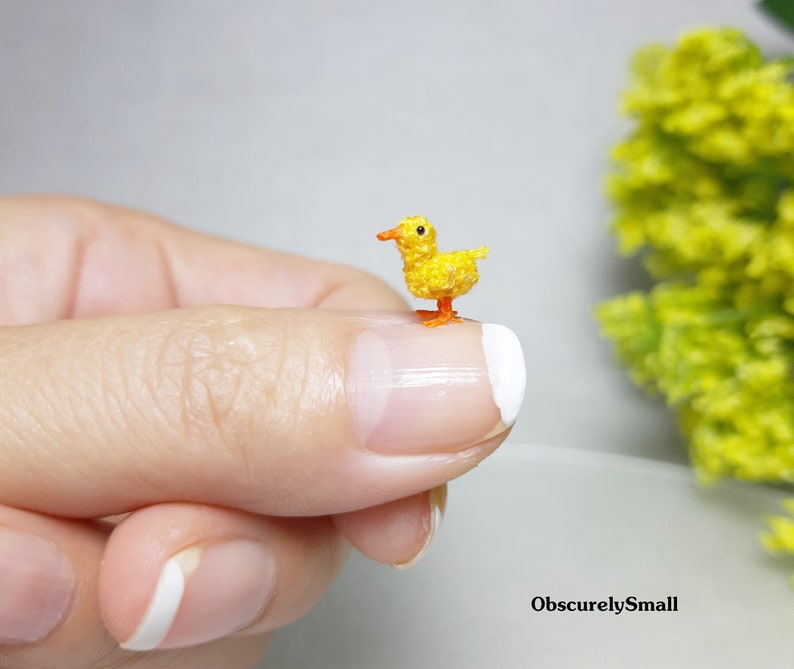 May include: A tiny crocheted yellow chick with orange feet and beak, perched on a finger.