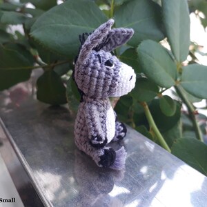Puede incluir: Un peque&ntilde;o burro de crochet gris sentado en una superficie plateada. El burro tiene ojos negros y una mancha blanca en el pecho.