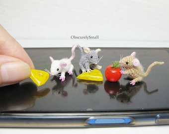 May include: Three crocheted mice figurines on a black surface. Two mice are eating yellow cheese wedges and one mouse is eating a red tomato.