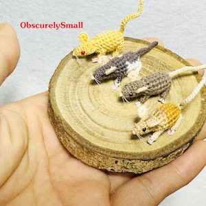May include: Four crocheted mice on a wooden base. The mice are in different colors, including yellow, gray, brown, and white. The base is a round piece of wood with a natural finish.