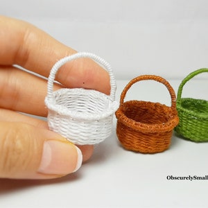 May include: Three miniature woven baskets in white, brown, and green, each featuring a rounded base and a single arched handle. The baskets are crafted from thin thread and are small enough to be held between fingers. The text ObscurelySmall is visible.
