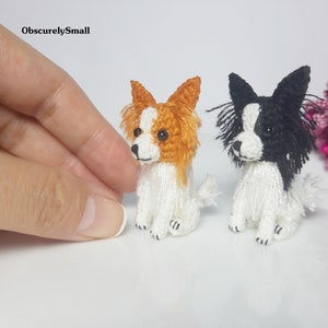 May include: Two small crocheted Papillon dogs, one with orange and white fur and the other with black and white fur. Both dogs are sitting with their heads turned to the side.