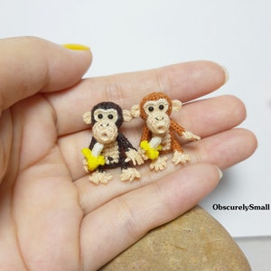 Könnte beinhalten: Zwei gehäkelte Affenfiguren, die winzige Bananen halten. Der Affe links ist braun und der Affe rechts ist orange.