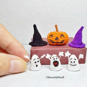 Pode incluir: Um conjunto de quatro decorações de Halloween de crochê, incluindo um chapéu de bruxa preto, um chapéu de bruxa roxo, uma abóbora laranja e três fantasmas brancos com diferentes expressões faciais.