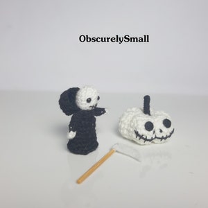 May include: A crocheted Grim Reaper figure in a black robe with a white face and a white pumpkin with a black face and a stitched smile. The Grim Reaper is holding a small white scythe.