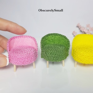 May include: Three miniature crocheted armchairs with wooden legs. The chairs are pink, green, and yellow.