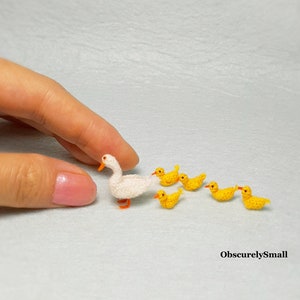 May include: A white crocheted duck with a yellow beak and orange feet, followed by five smaller yellow crocheted ducks.