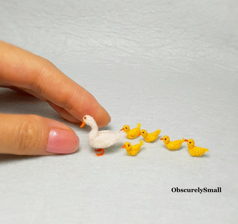 May include: A white crocheted duck with a yellow beak and orange feet, followed by five smaller yellow crocheted ducks.