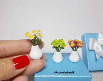 Puede incluir: Tres arreglos florales de ganchillo en miniatura en jarrones de cerámica blanca. Las flores son amarillas, verdes y rosas. Los jarrones están sobre una superficie azul claro con el texto "ObscurelySmall".
