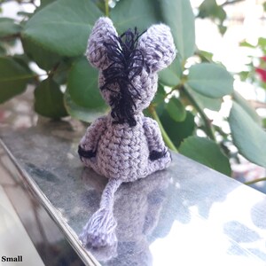 Puede incluir: Un peque&ntilde;o burro de crochet gris con hilo negro para la crin y la cola. El burro est&aacute; sentado en una superficie plateada.