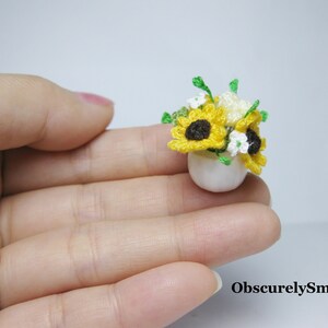 May include: A small white ceramic pot with a crocheted bouquet of yellow and white flowers. The flowers are crocheted to look like sunflowers and daisies.