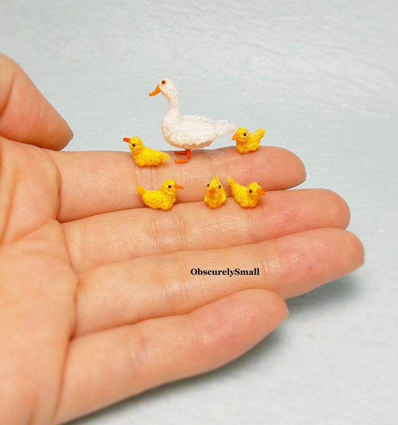 May include: A white crocheted duck with five yellow crocheted ducklings. The ducklings are arranged around the mother duck.