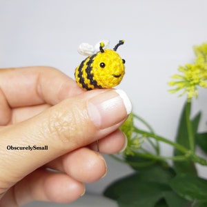 Op de afbeelding: Een kleine gehaakte bij met zwarte en gele strepen, witte vleugels en zwarte ogen. De bij wordt vastgehouden door een hand.