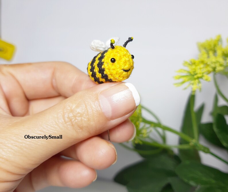 Op de afbeelding: Een kleine gehaakte bij met zwarte en gele strepen, witte vleugels en zwarte ogen. De bij wordt vastgehouden door een hand.
