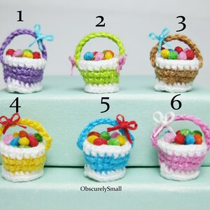 Pu&ograve; includere: Sei cestini in miniatura all'uncinetto pieni di caramelle colorate. I cestini sono di vari colori, tra cui viola, verde, marrone, giallo, blu e rosa. Ogni cestino ha un bordo in crochet bianco e un piccolo fiocco.