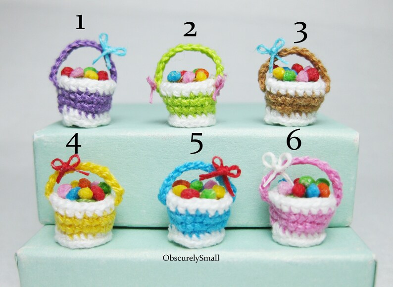 Pu&ograve; includere: Sei cestini in miniatura all'uncinetto pieni di caramelle colorate. I cestini sono di vari colori, tra cui viola, verde, marrone, giallo, blu e rosa. Ogni cestino ha un bordo in crochet bianco e un piccolo fiocco.