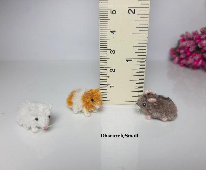 May include: Three small, handmade hamster plushies. The plushies are made of yarn and are about 1 inch tall. The plushies are white, brown and orange.