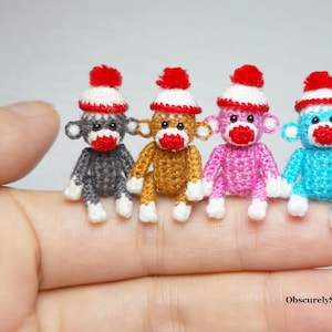 May include: Four miniature crocheted sock monkeys wearing red and white knit hats. The monkeys are gray, brown, pink, and blue.