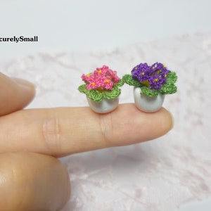 May include: Two miniature crocheted potted plants. One plant has pink flowers and the other has purple flowers. Both plants are in white pots.
