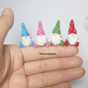 May include: Five miniature crocheted gnomes in different colours, including blue, pink, green, and red. Each gnome has a white beard and a pointed hat with white polka dots.