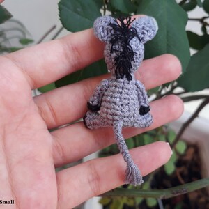 Puede incluir: Un peque&ntilde;o burro de crochet gris con orejas negras y cola negra. El burro est&aacute; sentado en una mano.