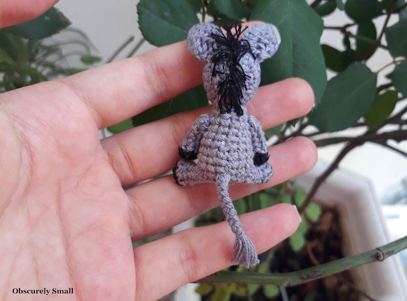 Puede incluir: Un peque&ntilde;o burro de crochet gris con orejas negras y cola negra. El burro est&aacute; sentado en una mano.