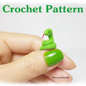 May include: A small green crocheted snake with a red tongue, sitting on a finger.
