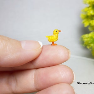 May include: A tiny crocheted yellow chick with orange feet and beak. The chick is sitting on a finger.