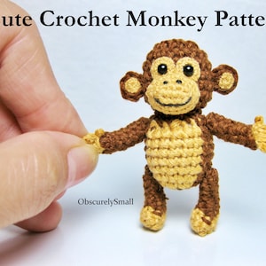 Może przedstawiać: Pluszowa zabawka małpka wykonana na szydełku, z brązowym futerkiem, żółtymi łapkami i czarnymi oczami. Małpka stoi na białym tle.