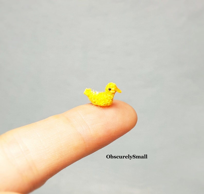 May include: A tiny yellow crocheted duckling, about the size of a fingertip, is perched on a finger.