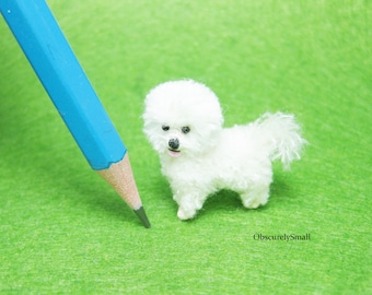 May include: A small white crocheted dog with black eyes and a pink tongue sticking out. The dog is sitting on a green surface with a blue pencil in the background.