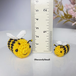 Op de afbeelding: Twee gehaakte hommels, een groter dan de andere, worden getoond naast een liniaal. De grotere hommel is geel en zwart met witte vleugels. De kleinere hommel is geel en zwart met witte vleugels. De liniaal is gemarkeerd in inches.