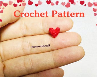 May include: A close-up of a small, red crocheted heart held in a hand. The heart is about the size of a fingernail. The text "ObscurelySmall" is visible below the heart.