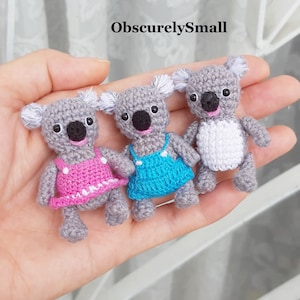 May include: Three crocheted koala bears wearing different coloured dresses. The koala on the left is wearing a pink dress, the koala in the middle is wearing a blue dress, and the koala on the right is wearing a white dress.