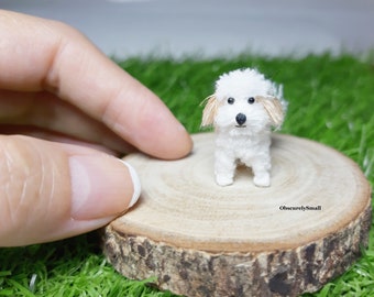 May include: A small white crocheted dog with brown ears sitting on a wooden slice. The dog is about 5 cm tall and has black eyes and a black nose.