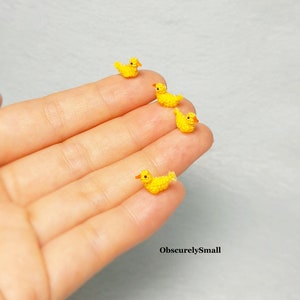 May include: Four tiny crocheted yellow ducklings with orange beaks and feet, arranged in a line on a hand.